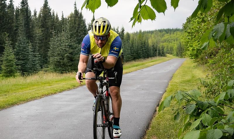 Cyklist på tempocykel cyklar på väg iblandat landskap.
